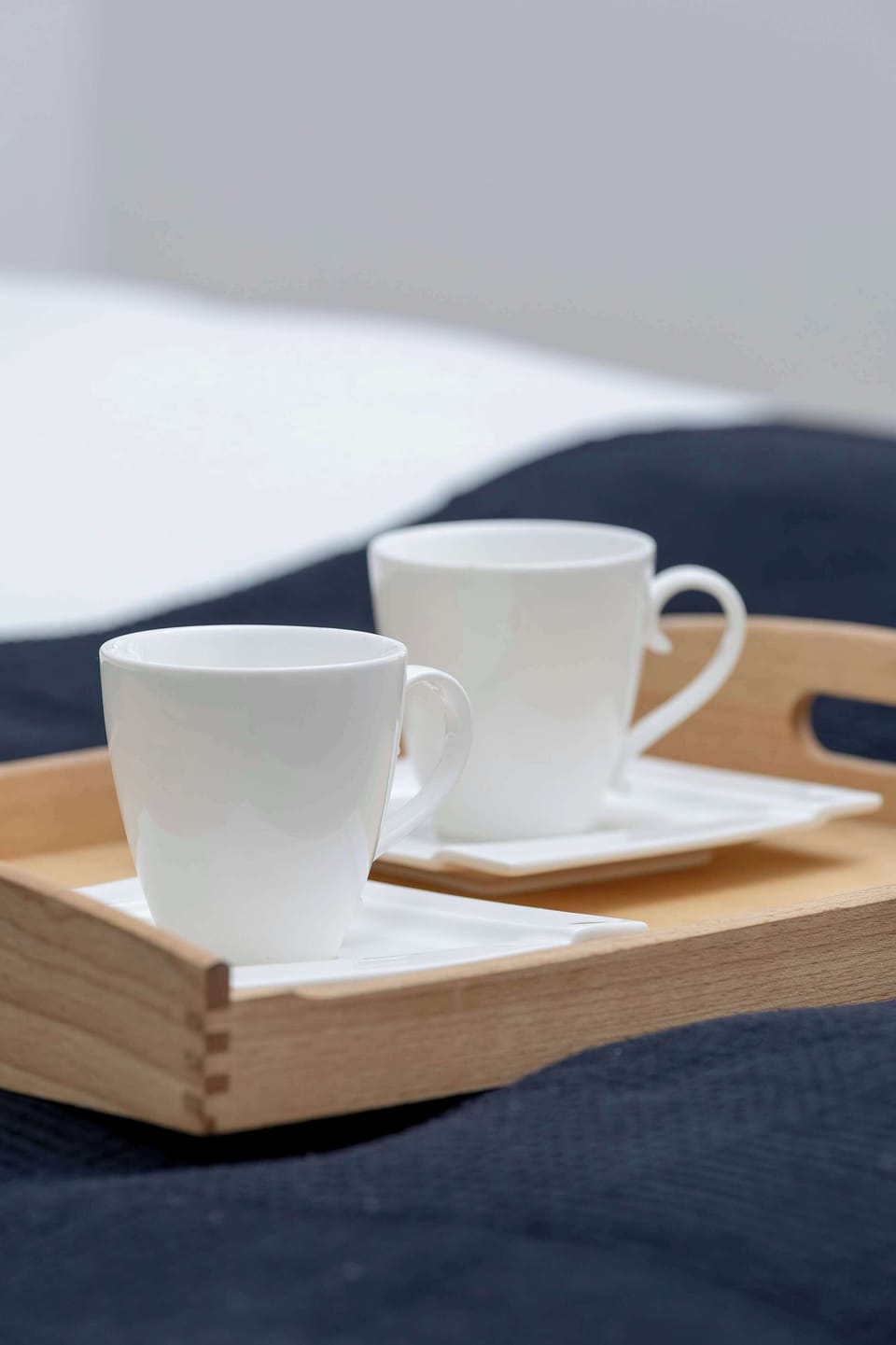 This close-up focuses on the wooden tray and white cups used for serving tea or coffee. The texture of the dark blue fabric underneath adds depth to the simple composition.