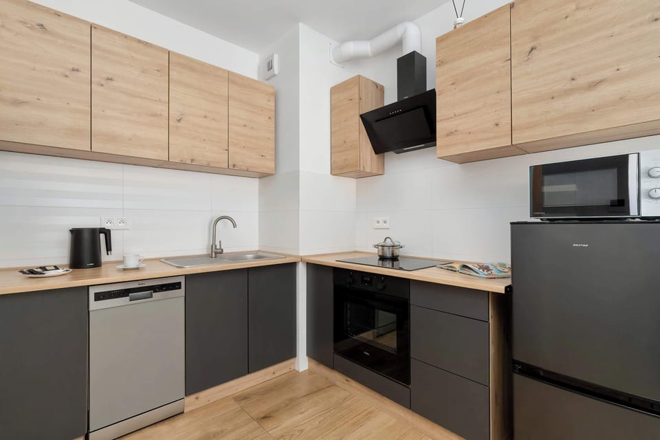 A modern kitchen with light wood cabinets, black countertops, and built-in appliances arranged in an L-shape.