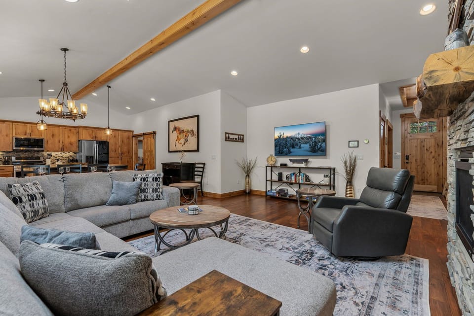 Relax in your spacious living room with plush sofas, warm wood accents, and stunning mountain views on the TV.