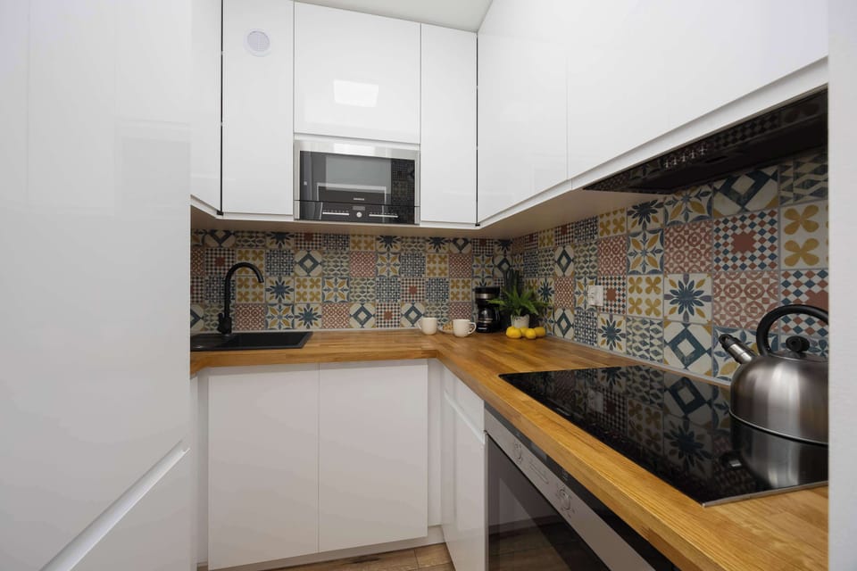 A modern kitchen with white cabinets and a patterned backsplash. Wooden countertops add warmth to the space.