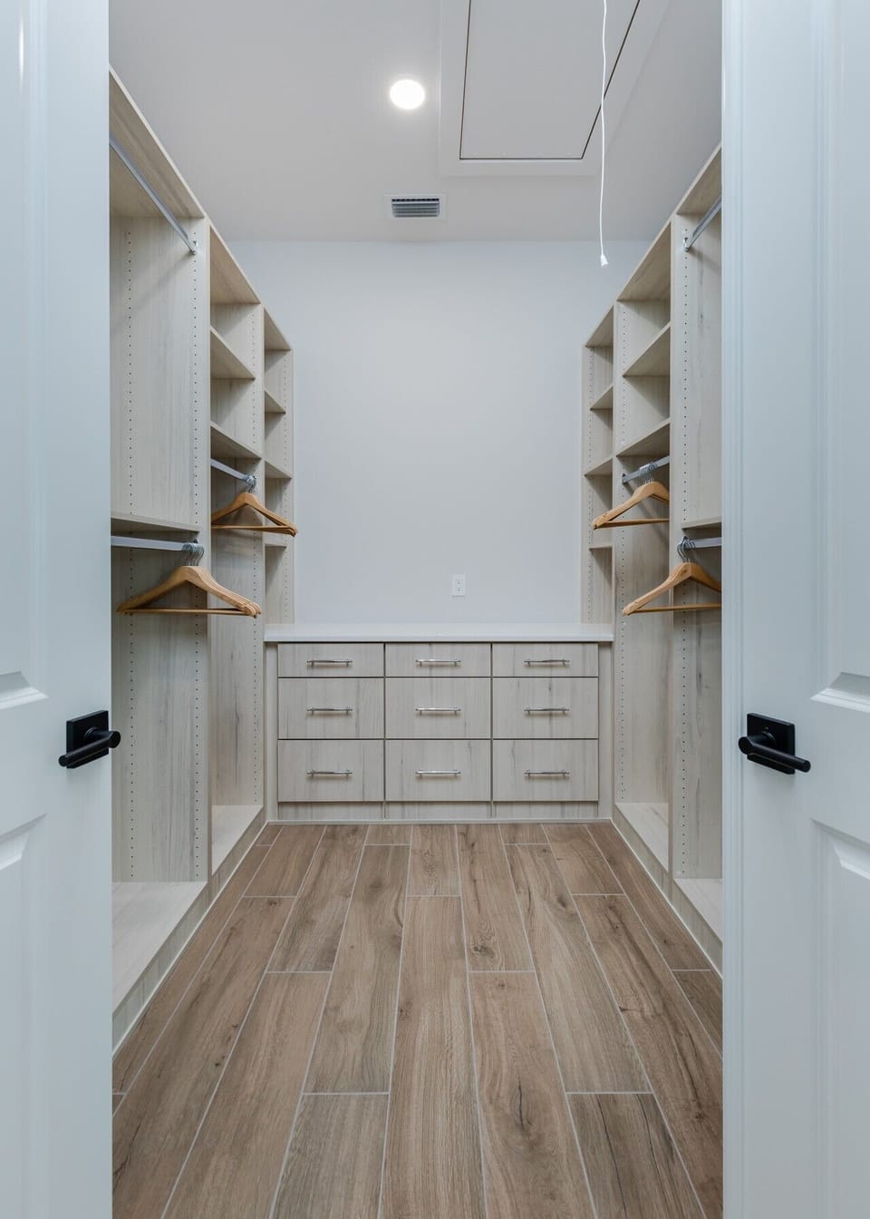 Spacious walk-in closet with built-in shelving, hanging storage, drawers, and wood-look tile flooring.