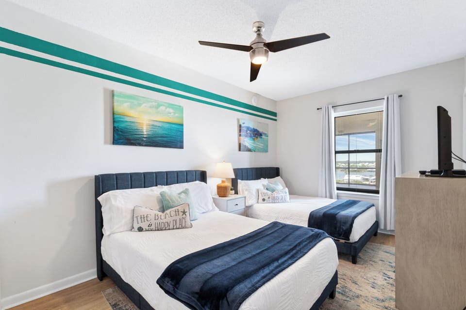 Bright coastal bedroom with 2 plush beds, TV, and water views.