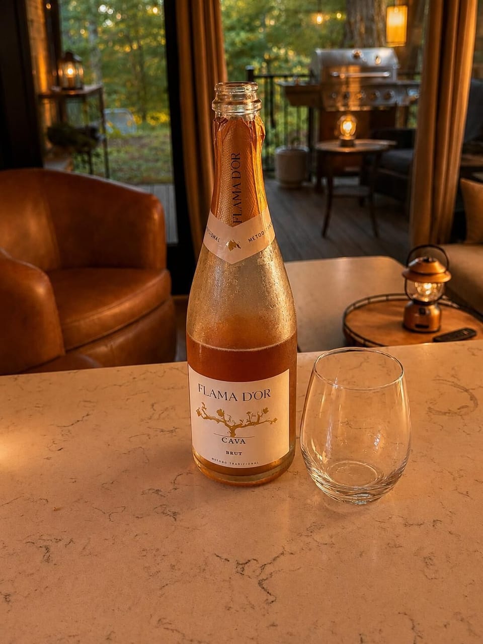 Marble countertop holds a chilled bottle of Flama D’Or cava and a clear stemless glass, with leather chairs nearby.