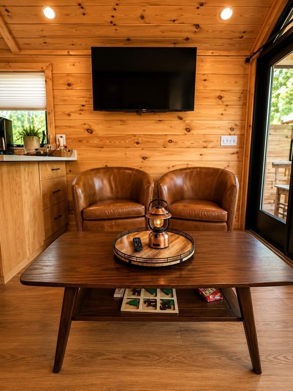 Wall-mounted flat screen TV above two cognac leather club chairs and a dark wood coffee table with a copper lantern.
