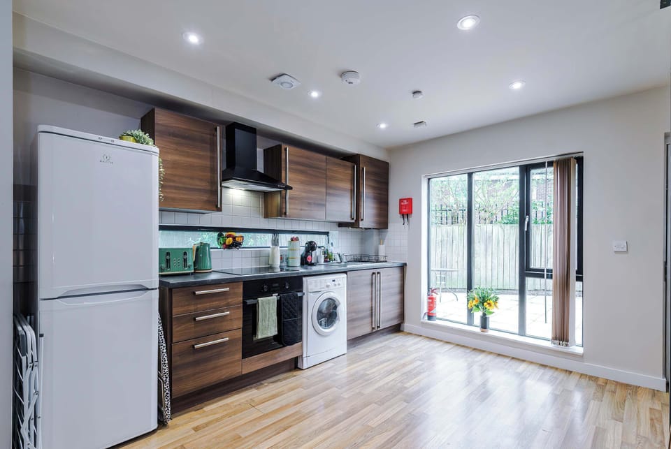 Contemporary kitchen featuring stylish wood cabinets, oven, microwave, and washing machine. Natural light from the glass doors enhances the warm tones, offering guests a practical yet inviting space.
