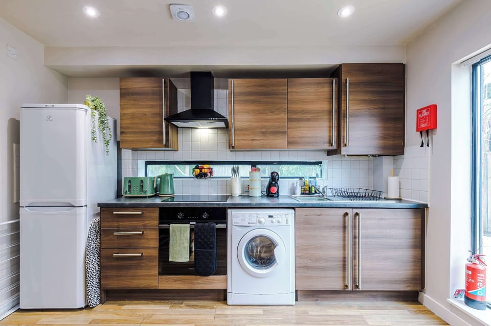 Modern kitchen with sleek wooden cabinets, black countertop, and integrated appliances. Natural light, recessed lighting, and thoughtful layout make this space efficient and welcoming for cooking and laundry needs.
