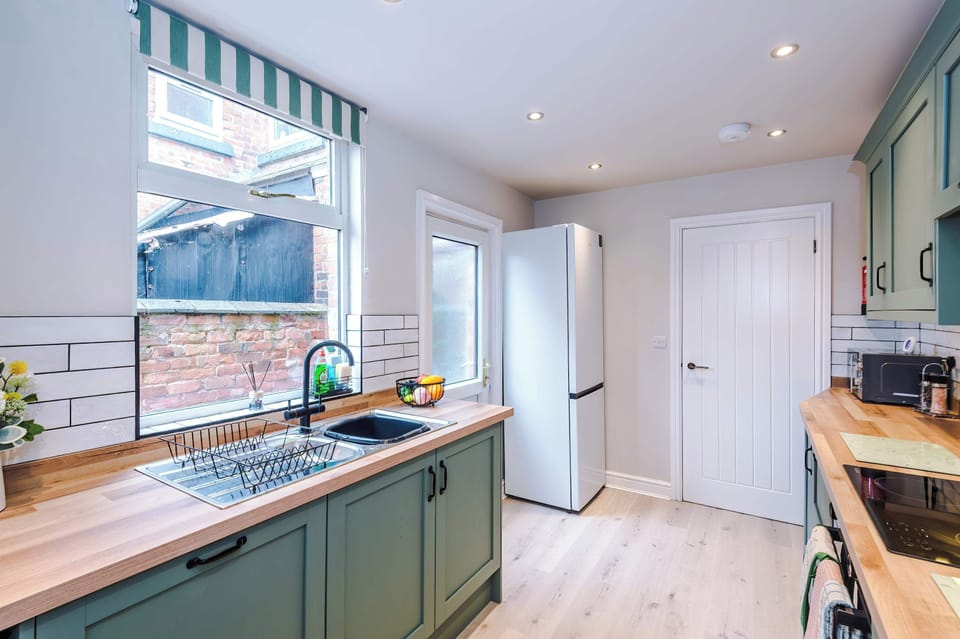 A clean, functional kitchen space with gray cabinets, wooden countertops, white subway tile backsplash, and everyday appliances neatly arranged, blending practicality with contemporary design and warm lighting.