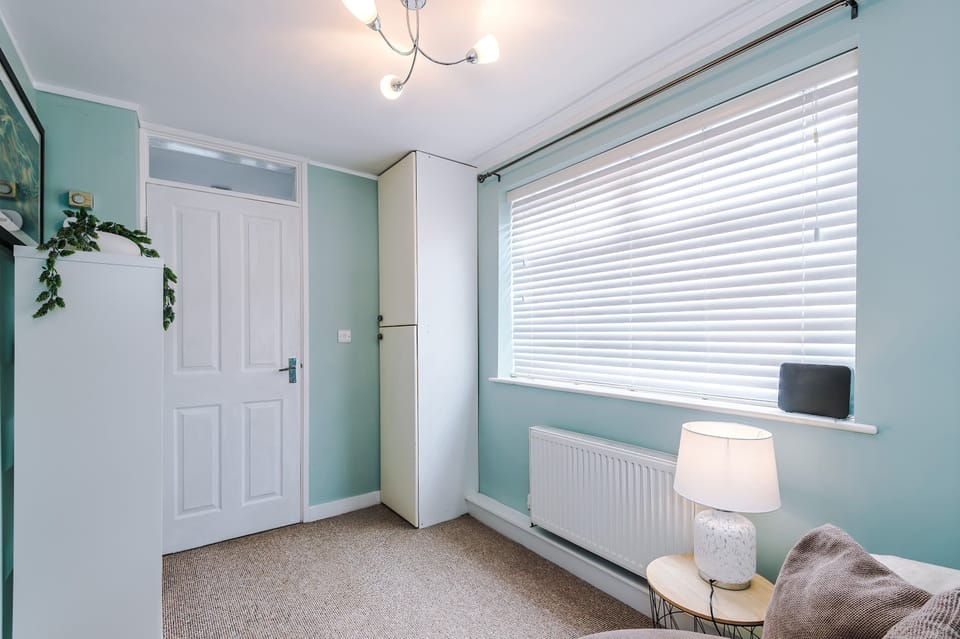 Contemporary comfort: a light blue reading nook with bookshelf and framed art opens into a lounge with sofa, coffee table, and TV. Warm lighting ties the rooms together in a stylish, cozy design.