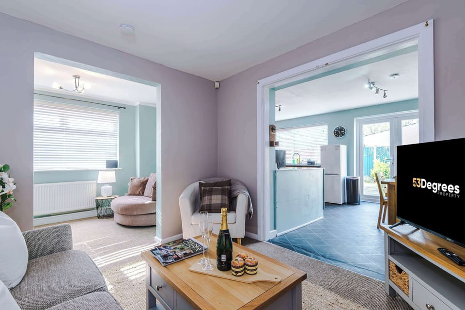 Contemporary comfort: gray sofa with cushions, wooden coffee table set with champagne, and abstract art above. A mirror and flowers bring charm to this bright, stylish living space.