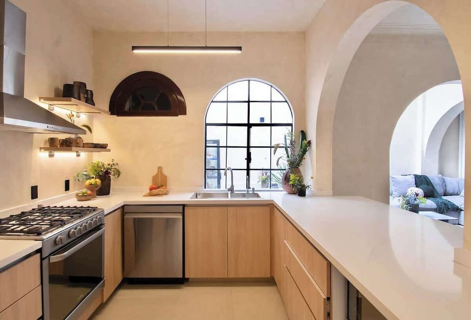 A warm, open cooking area with clean lines and generous counter space. Natural light, soft arches, and thoughtful finishes create a seamless connection between daily routines and shared moments.