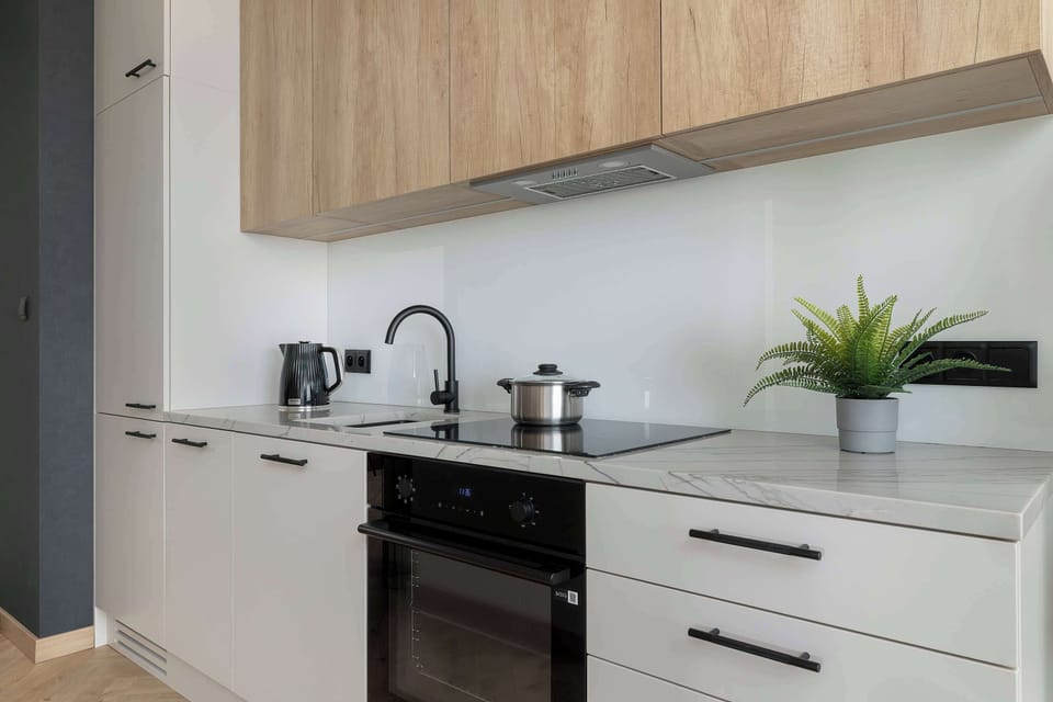 A sleek kitchenette with white cabinets, a built-in oven, and a modern countertop. Wooden upper cabinets add warmth, while the minimalist design keeps the space clean and functional.