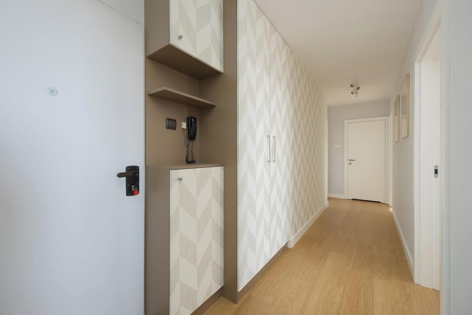 A minimalist hallway transition leads from the entry area toward the main living spaces. A tall white wardrobe with a textured pattern provides ample storage along the wall.