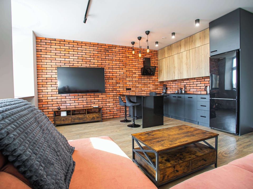 A cozy lounge area featuring a brick accent wall, a mounted TV, and a wooden coffee table. The combination of industrial and warm elements gives the interior a welcoming, urban character.