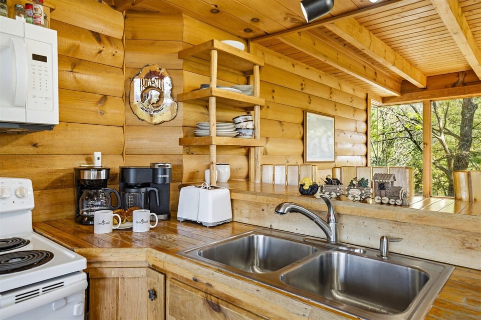 Step into your rustic cabin kitchen where morning coffee awaits. Wood beams and open shelving create cozy charm for memorable meals.