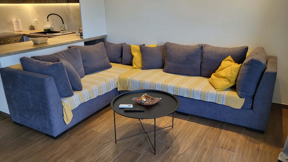 The living room from a wider angle, showing the full run of the L-shaped sofa, the TV unit, and the warm tone the lighting gives the space in the evenings.