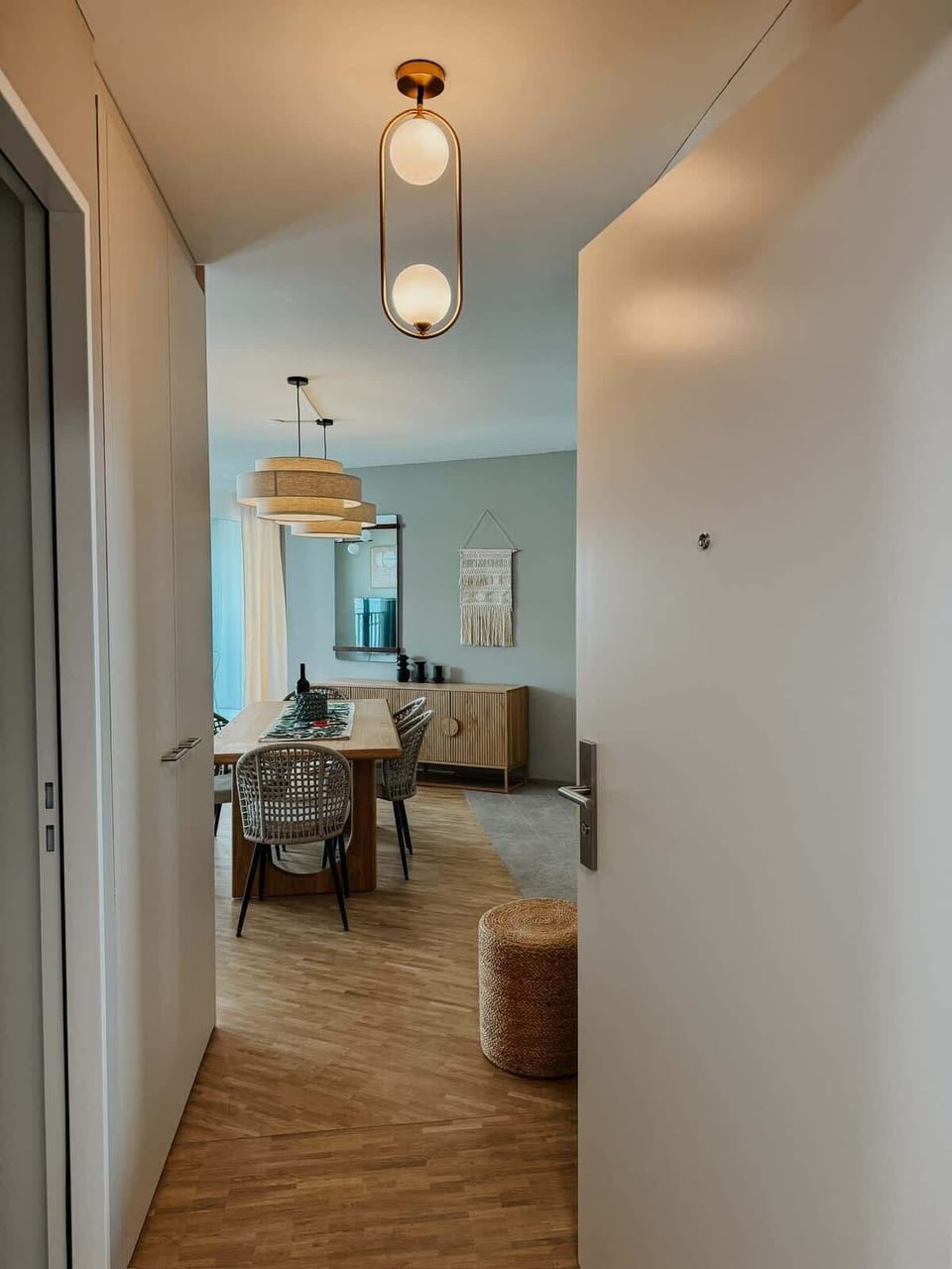 Willkommen in deinem stilvollen Zuhause auf Zeit! Schon beim Eintreten empfängt dich ein heller Flur mit Designleuchte und direktem Blick in den offen gestalteten Wohn- und Essbereich mit warmem Holz und natürlichen Materialien.