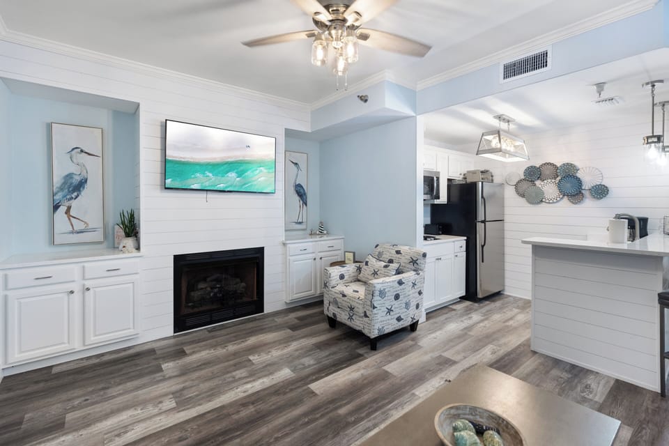 Unwind in your coastal-inspired living space featuring a cozy fireplace and modern kitchen perfect for preparing meals during your stay.