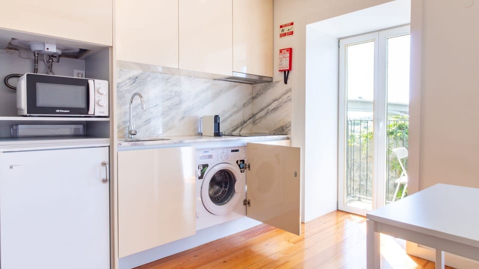 Enjoy the convenience of a compact kitchen complete with a built-in washer, allowing you to refresh your clothes after a day of exploring, all while bathed in natural light from the balcony. #CompactKitchen #WasherConvenience #NaturalLight #BalconyDoor #L