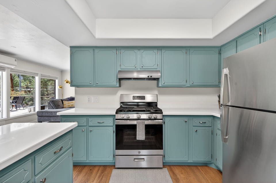 Modern kitchen featuring stainless steel range, vent hood, and refrigerator, complemented by quartz countertops and custom teal cabinets for a fresh contemporary look.
