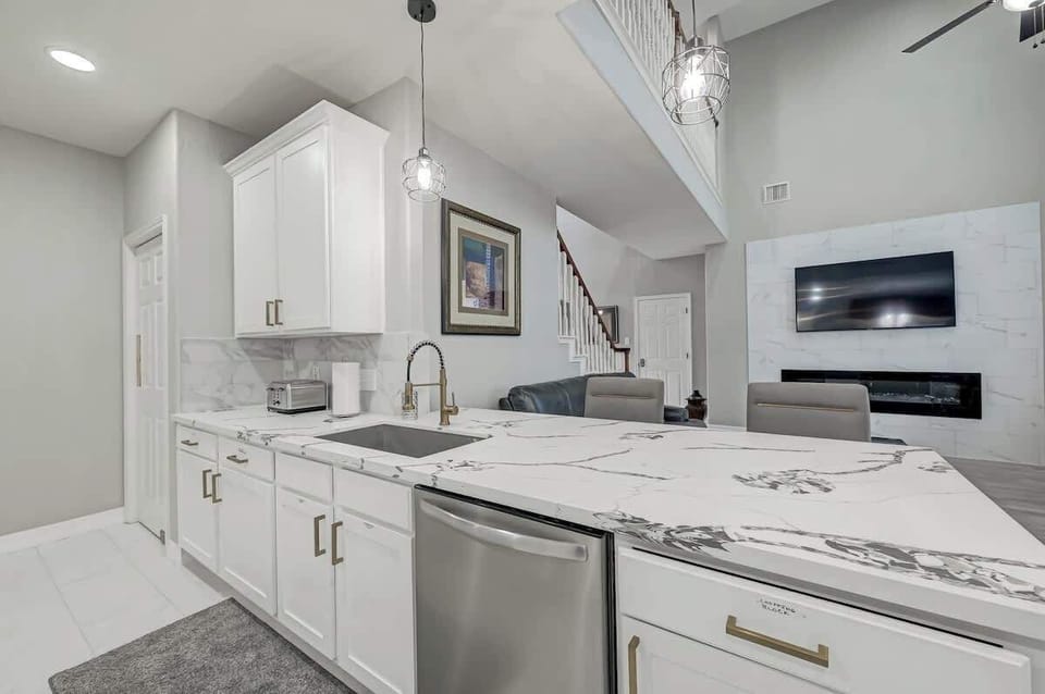 Elegant breakfast bar with marble design, a dish washer, pendant lighting, and open sightlines to the living room.

