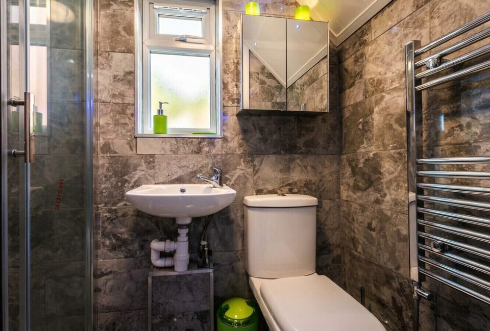 A fully tiled shower room with a walk-in enclosure, chrome heated towel rail, mirrored cabinet, and natural light from a frosted window.