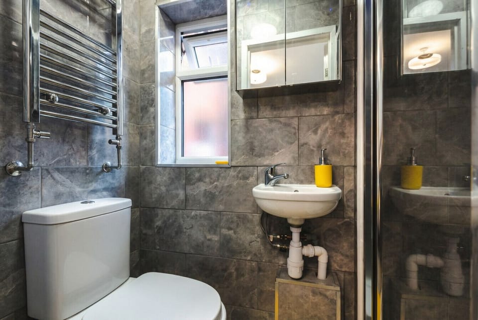 The bathroom features full marble-effect tiling, a chrome heated towel rail, walk-in shower enclosure, and a mirrored storage cabinet.