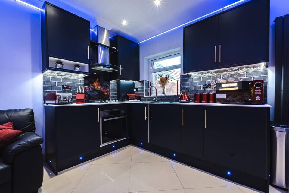 Cook in style in the dark high-gloss kitchen, fully equipped with a built-in oven, extractor hood, gas hob, and striking blue LED under-cabinet lighting.