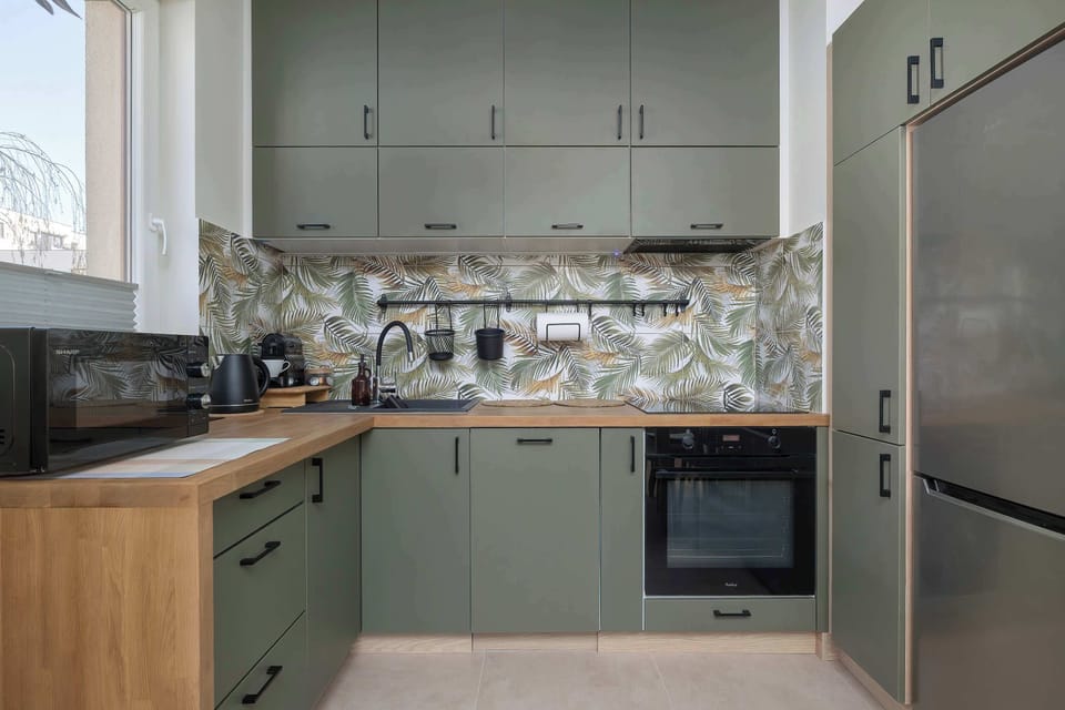 A stylish kitchenette with muted green and wood cabinetry, complemented by a patterned backsplash. Built-in appliances and clean lines make the space both functional and visually appealing.