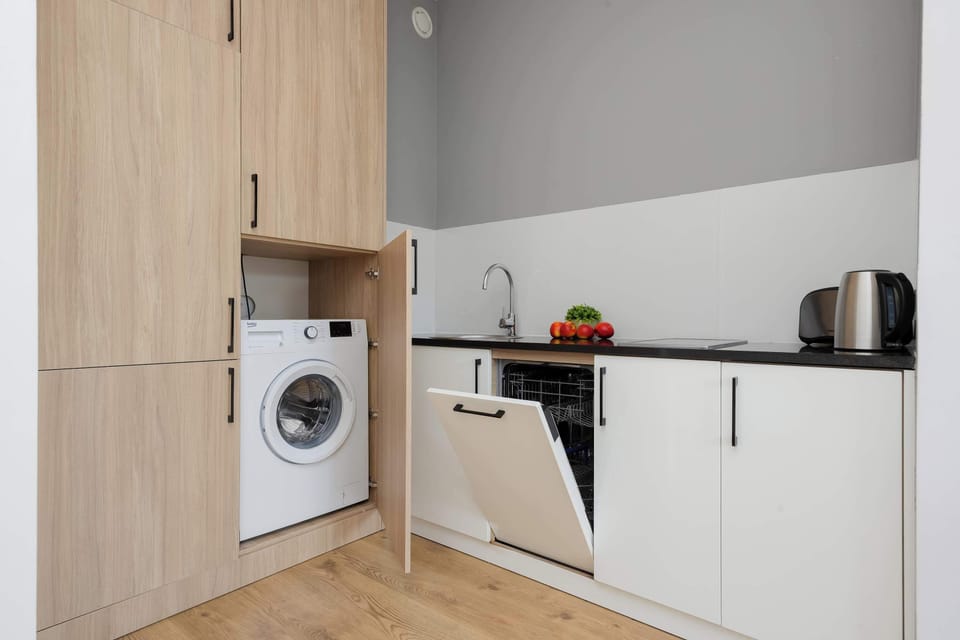 An open door revealing a compact laundry setup with a washing machine and storage space within a light wooden cabinet.