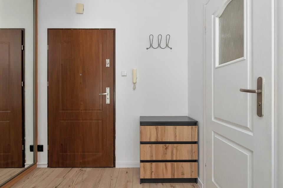 An apartment entrance with a wooden front door, coat hooks, and a compact storage bench.
