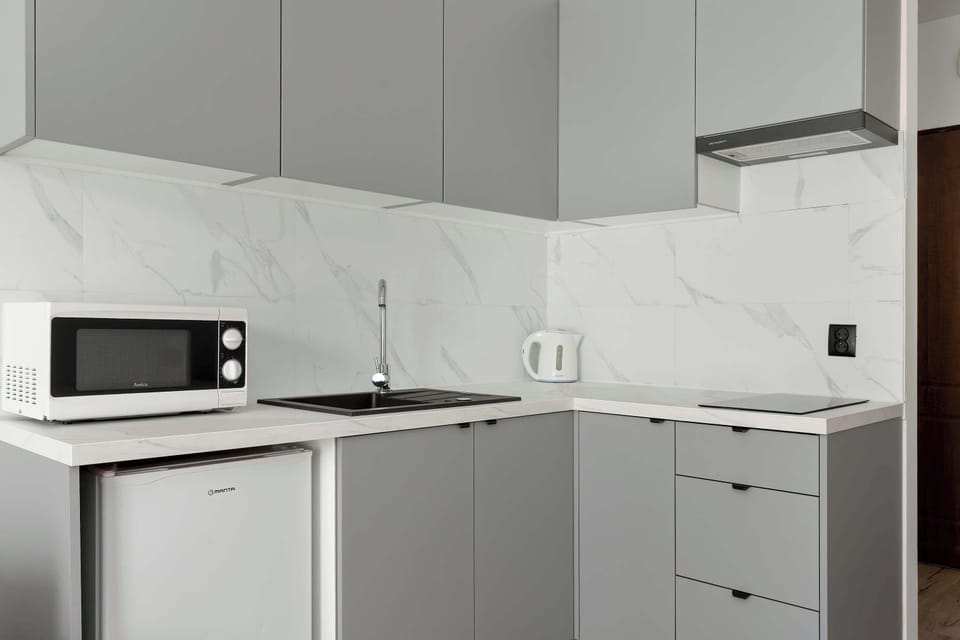 A compact kitchen corner with white cabinets, a microwave, kettle, and clean countertop space.