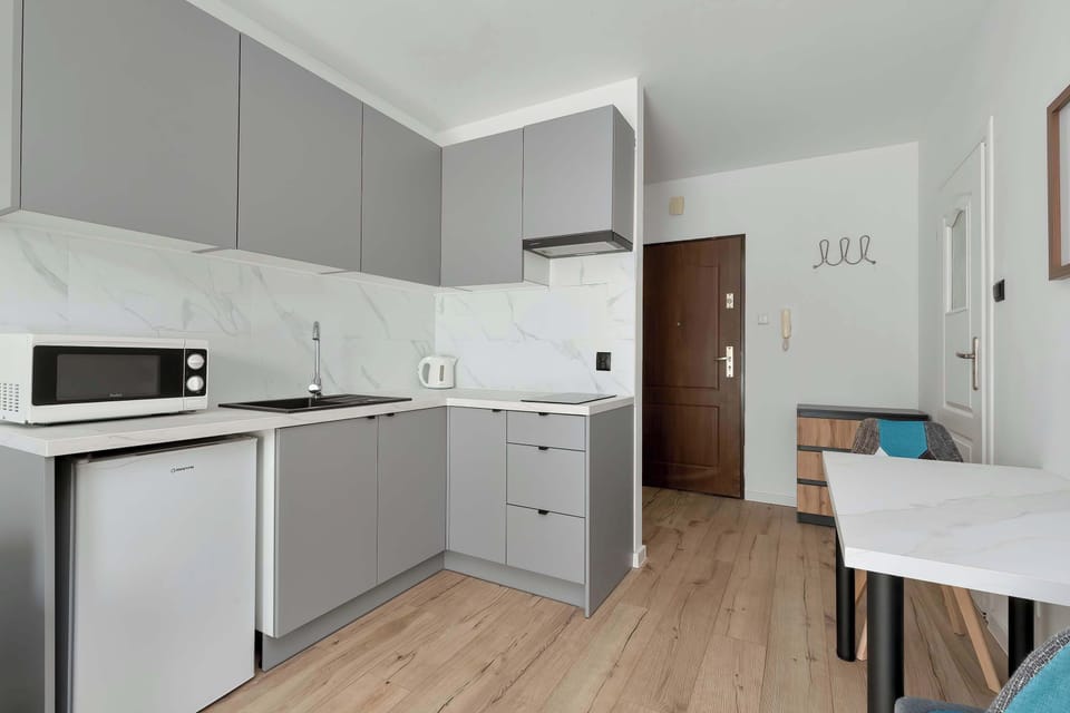 A clean, modern kitchenette with white cabinetry, appliances, and a small dining table nearby.