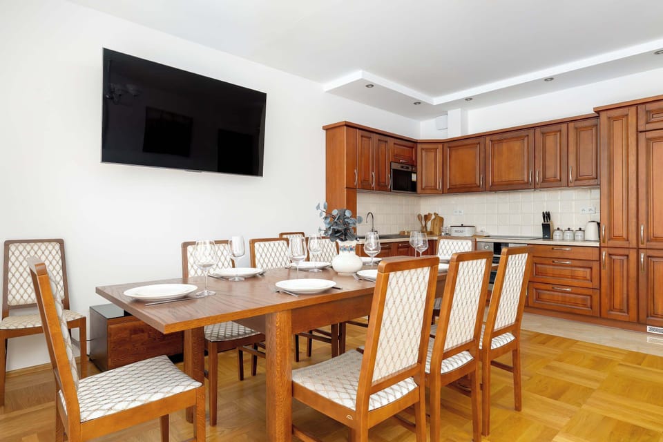 The dining area features a sturdy wooden table surrounded by elegant chairs with upholstered backs. In the background, the kitchenette's wooden cabinetry adds a sense of traditional craftsmanship to the home.