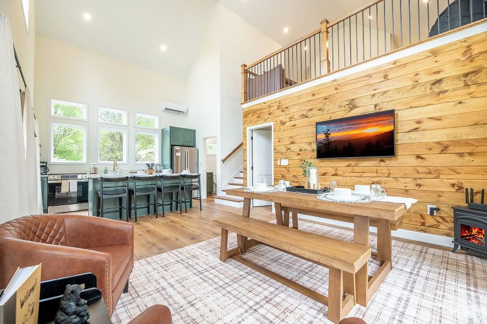 Relax in this stunning open-concept living space where rustic wood meets modern comfort, featuring vaulted ceilings and cozy fireplace warmth.