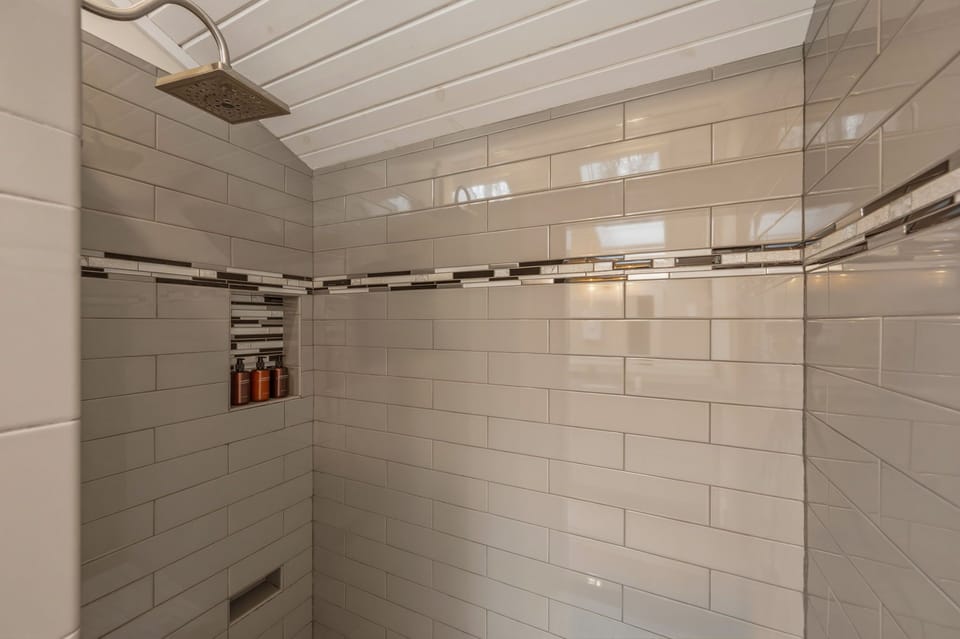 Spa-style walk-in shower with sleek subway tile, a rainfall shower head, and a built-in niche stocked with amenities.