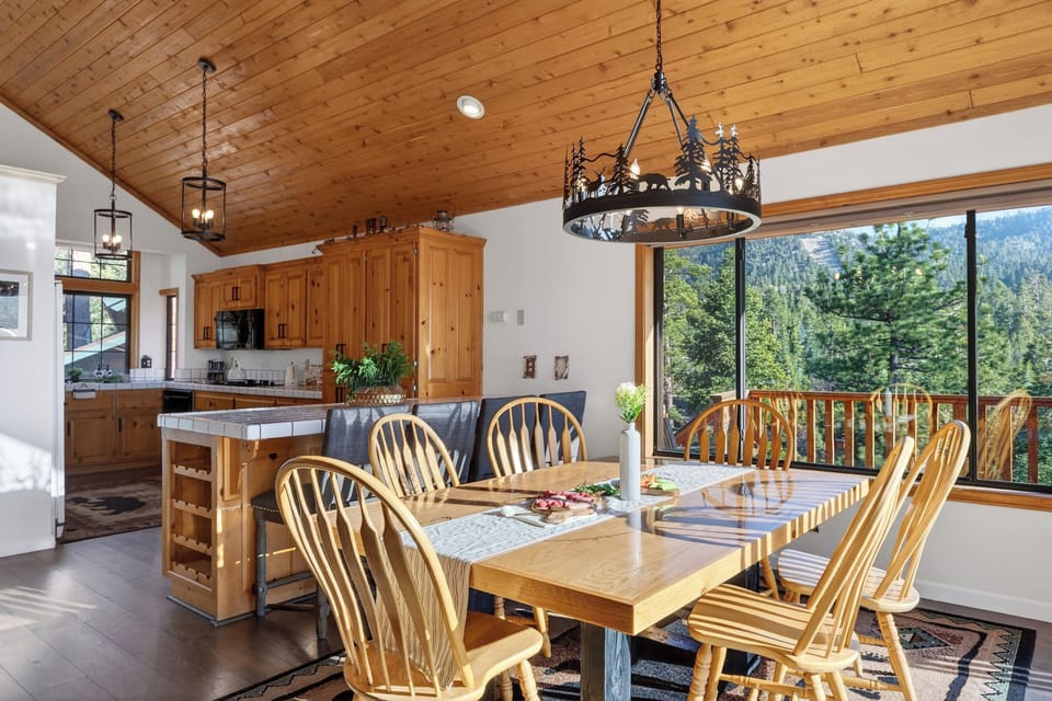 Cozy cabin dining area with wood‑beam ceilings, nature‑inspired lighting, and mountain views through large windows.