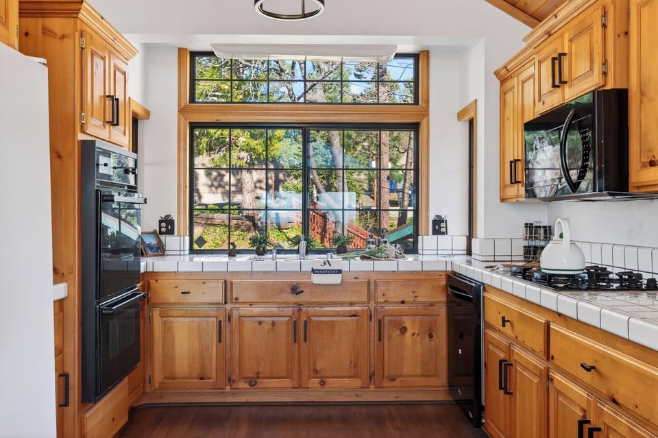Warm, wood‑toned kitchen with vaulted ceilings, rustic lighting, and mountain views through floor‑to‑ceiling windows.