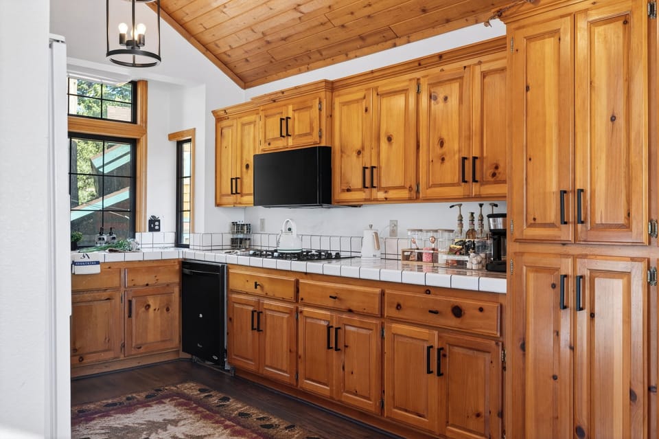 Warm, wood‑toned kitchen with vaulted ceilings, rustic lighting, and mountain views through floor‑to‑ceiling windows.