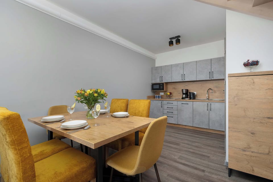 A functional dining space includes a wooden table set for four people, positioned near a modern kitchenette with grey cabinetry.