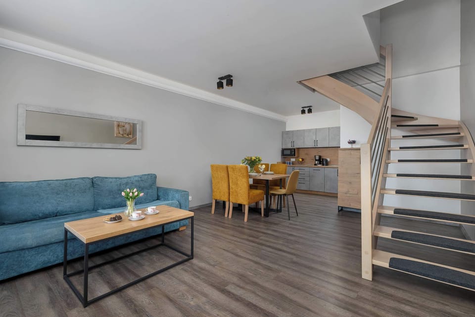 A wide-angle living room view captures the teal sofa and the wooden staircase leading to the upper floor of the duplex.