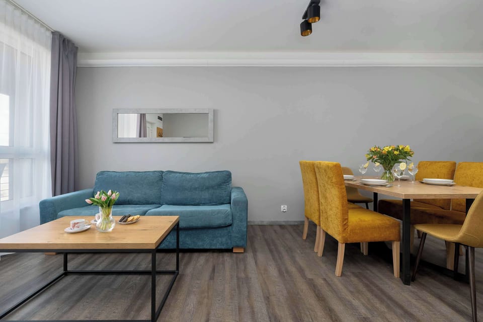 A cozy lounge perspective shows the teal sofa and dining table from a distance, highlighting the spacious feel of the main living area.