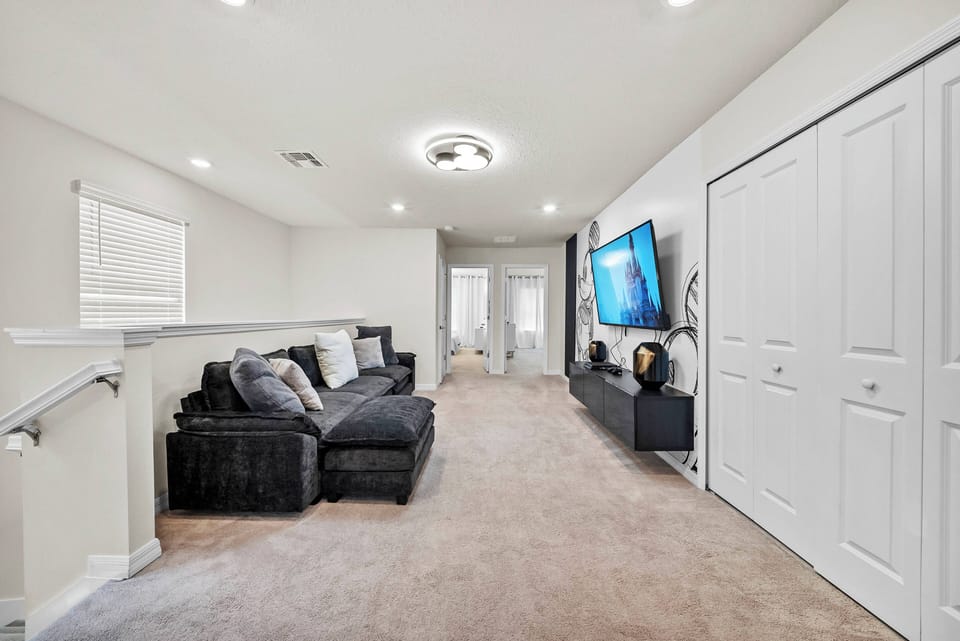 Welcome to a cozy living area with a plush dark sectional sofa, light-colored walls for a spacious feel, soft carpeting, and stylish lighting, creating a warm ambiance perfect for unwinding after your adventures.