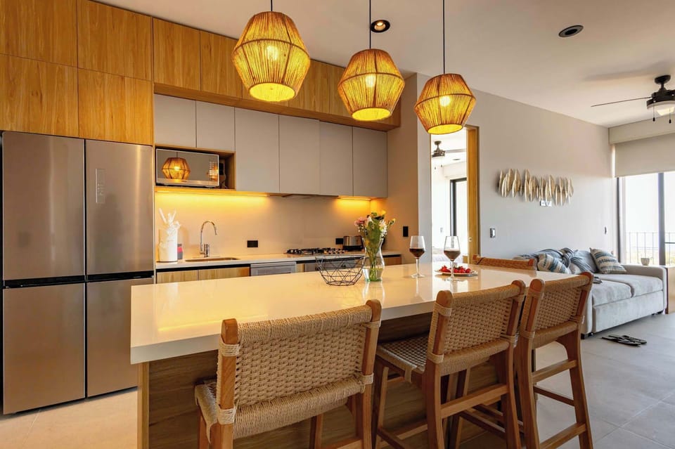 Sleek kitchen & dining space w/ wood cabinetry, island seating & warm pendant lights