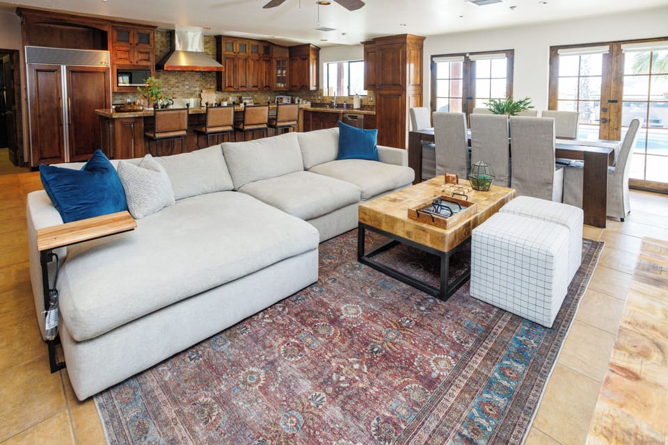 The open concept great room includes a comfy sitting area, kitchen with bar seating, a dining area and doors to the backyard paradise.