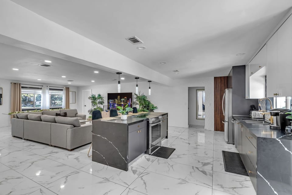 Cook and connect in our chef's kitchen featuring a stunning marble island, gold accents, stainless appliances, and pendant lighting — all flowing seamlessly into the spacious living area. 