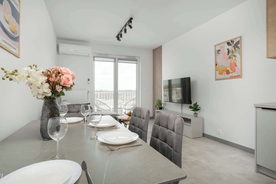 A formal dining area is set with a grey table and matching upholstered chairs. The table is neatly arranged with plates and a decorative floral centerpiece.