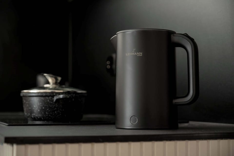 A modern kitchen detail featuring an electric kettle placed on a dark countertop. The minimalist setup with a neutral color palette emphasizes functionality and clean design.