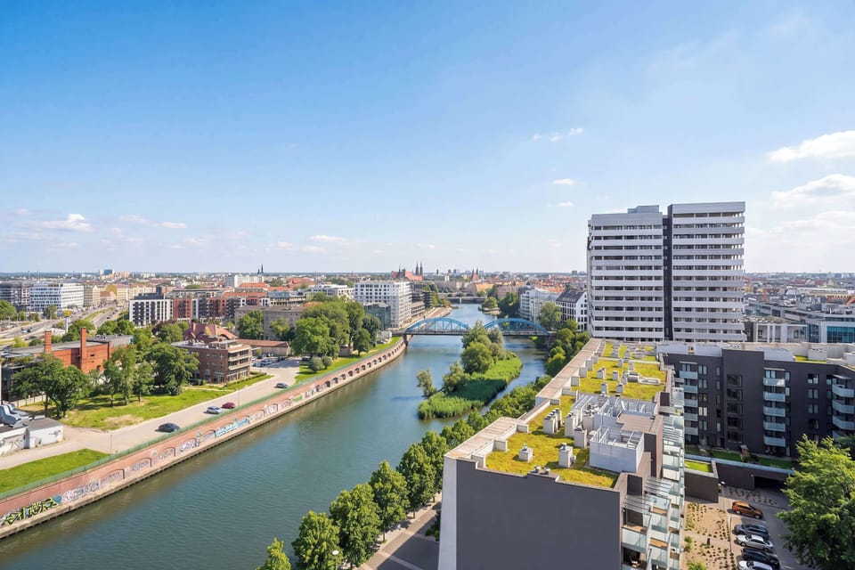 An elevated view overlooking a river and cityscape with modern buildings and greenery. The scenery adds a sense of openness and connection to the urban surroundings.