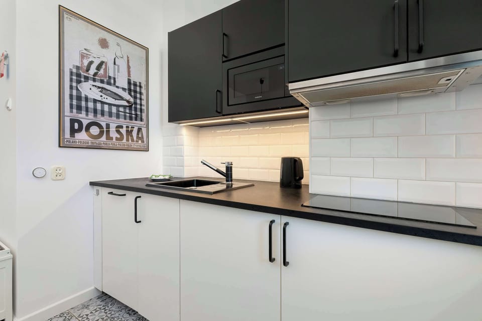 A sleek kitchenette workspace features a black countertop and a white tiled wall. A framed "Polska" poster is mounted on the wall, adding a touch of local character to the decor.