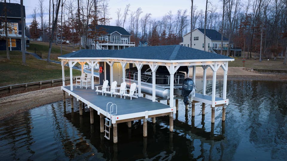 Boathouse - Adirondack chairs on the dock deck, the pontoon on the lift, and the boat garage door lit at dusk.